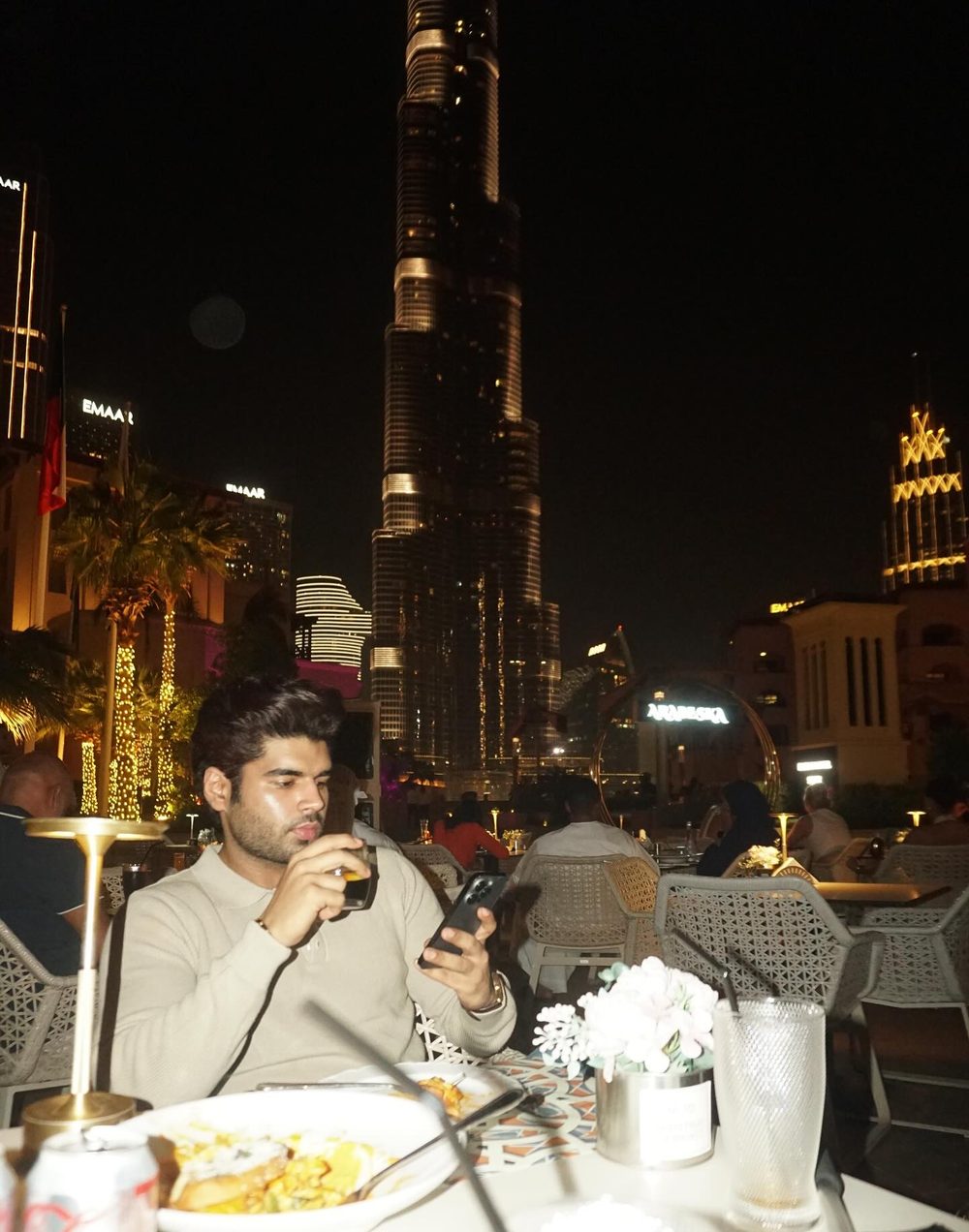 Man at a restaurant table at night with the Burj Khalifa lit up behind him